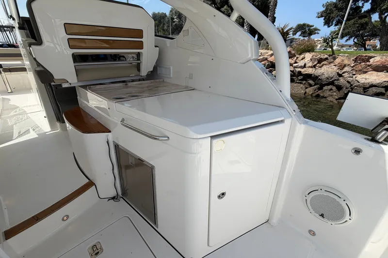 Slide: The Image of 2019 Pursuit DC 365 Dual Console boat interior with seating and storage, docked by rocky shoreline. - 19