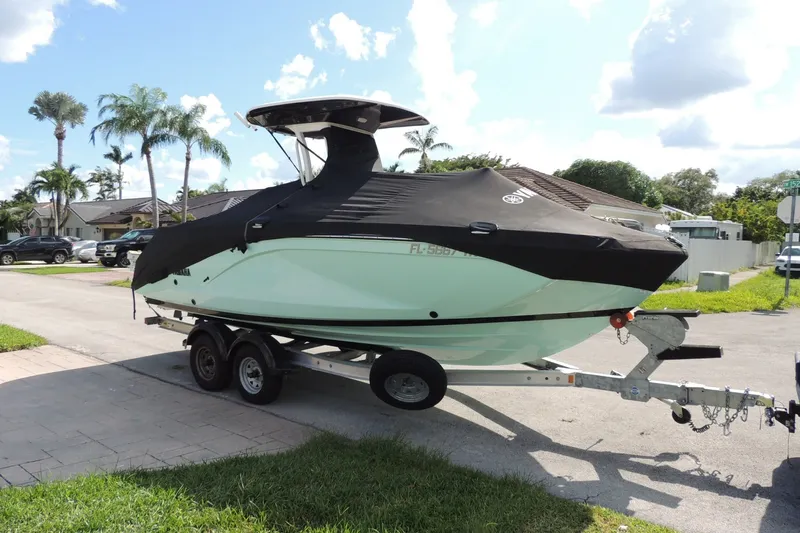 Slide: The Image of 2023 Yamaha Boats 222 FSH Sport E on trailer, covered, parked in suburban area. - 1