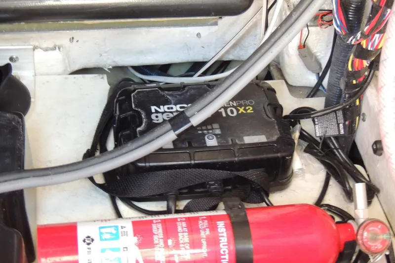 Slide: The Image of 2023 Yamaha Boats 222 FSH Sport E engine compartment with NOCO Genius battery charger and fire extinguisher. - 26