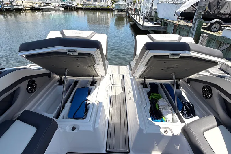 Slide: The Image of 2023 Yamaha Boats 275SE with open storage compartments docked by waterfront homes. - 22
