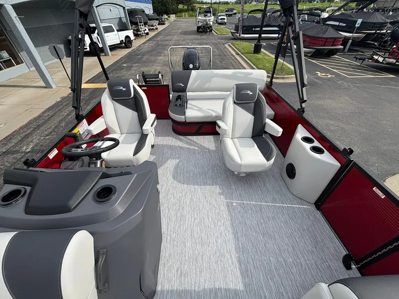 Slide: The Image of The image shows the interior of a 2027 Bennington 21 S1SB SPS pontoon boat. It features gray and white seating with red accents, parked in a lot. - 17
