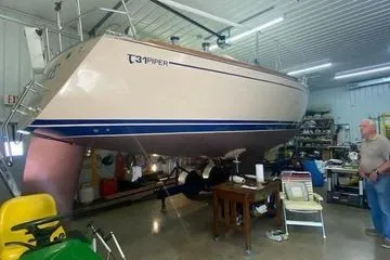 Slide: The Image of A 1992 Tartan 3100 in a workshop. The hull is cream-colored with blue stripes. - 17