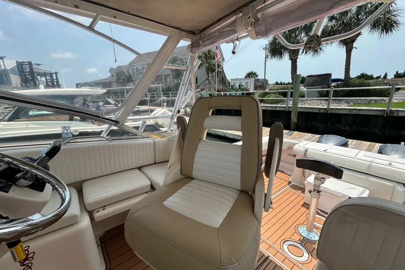 Slide: The Image of 2005 Grady-White Express 330 boat interior with seating and steering wheel, docked near palm trees. - 12