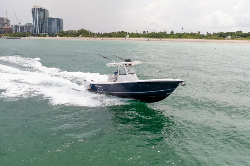 Slide: The Image of 2023 Regulator 28 Forward Seating boat cruising near a beach with city skyline. - 7