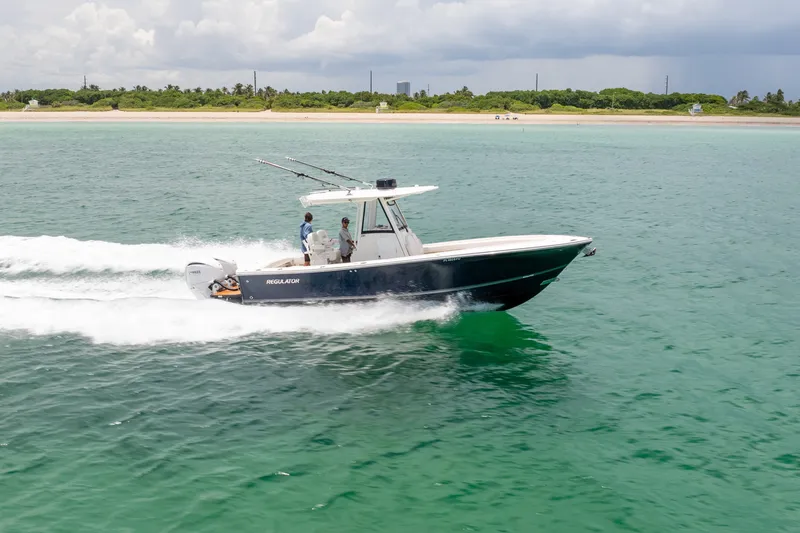 Slide: The Image of 2023 Regulator 28 Forward Seating boat cruising on clear turquoise water near a lush shoreline. - 1