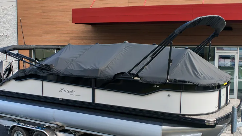 The Image of A 2027 Barletta Aria 24UC pontoon boat with a gray cover on a trailer. - 1