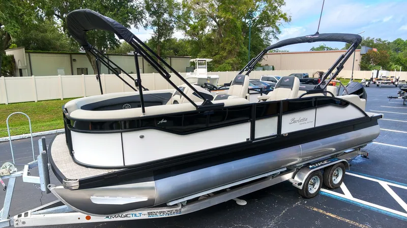 Slide: The Image of A 2027 Barletta Aria 24UC pontoon boat on a trailer in a parking lot. - 2