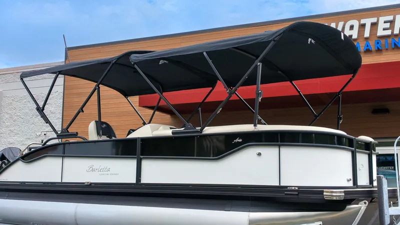 Slide: The Image of The image shows a Barletta Aria 24UC pontoon boat with a black canopy in front of a building. - 22