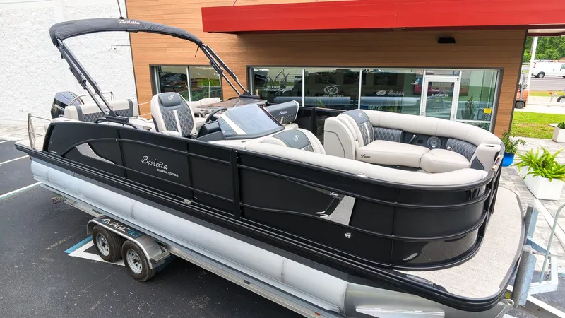 The Image of A sleek 2027 Barletta Lusso 25UE pontoon boat on a trailer in front of a modern building. - 1