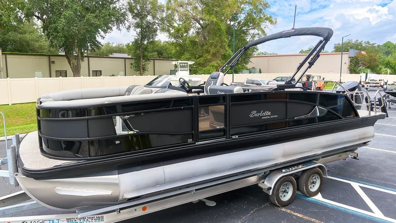 The Image of A sleek 2027 Barletta Lusso 25UE pontoon boat sits on a trailer in a parking lot. - 1