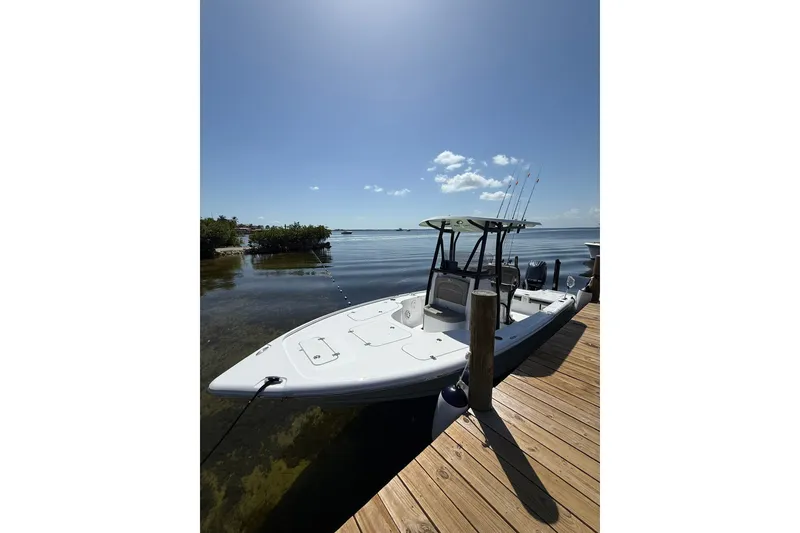 Slide: The Image of 2025 Sea Hunt BX22BR boat docked by a serene waterfront under a clear blue sky. - 7