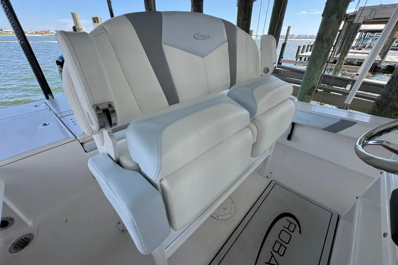 Slide: The Image of 2025 Robalo 226 Cayman boat seating with white and gray upholstery, docked by the water. - 24