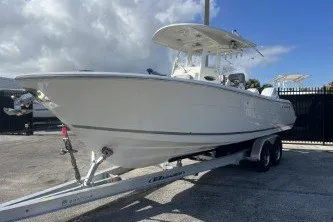 Slide: The Image of 2024 Cobia 262 Center Console boat on trailer, parked outdoors under cloudy sky. - 2