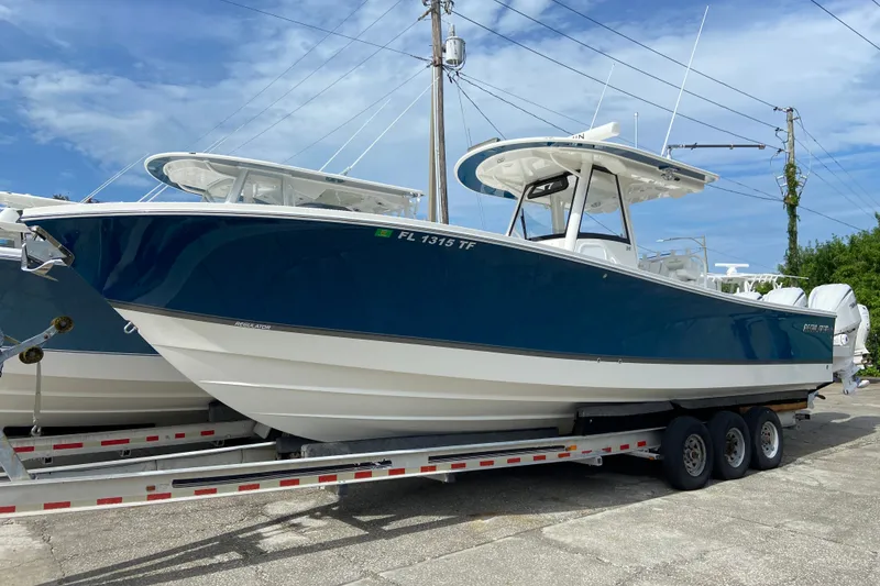 Slide: The Image of 2022 Regulator 34 boat on trailer, blue and white design, parked outdoors. - 12