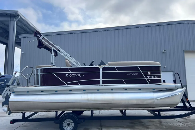 The Image of 2021 Godfrey Sweetwater 2086 C pontoon boat on trailer, parked near a metal building. - 2