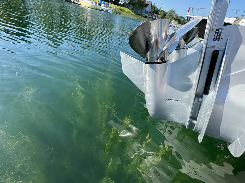 Slide: The Image of A shiny boat engine in the water, surrounded by aquatic plants, with a calm shoreline in the background. - 48