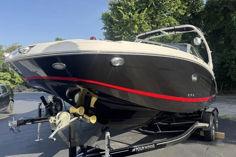 Slide: The Image of 2019 Four Winns HD240 Surf boat on trailer, black with red stripe, parked outdoors. - 1