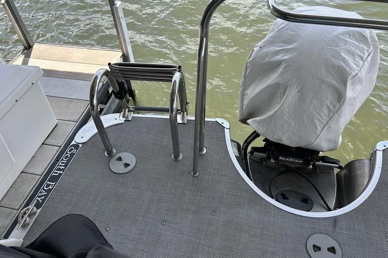 Slide: The Image of 2015 South Bay 524 SLTT boat deck with motor cover and ladder by the water. - 5