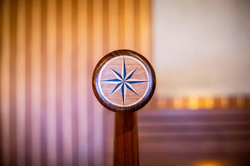 Slide: The Image of A wooden helm with an inlaid compass star design, surrounded by warm wood tones. - 49