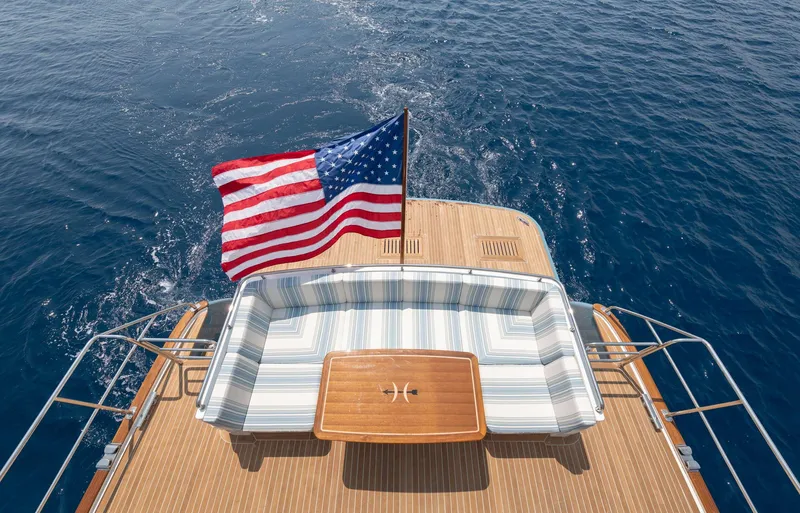 Slide: The Image of The stern of a yacht with an American flag, striped sofa, and wooden table. - 15