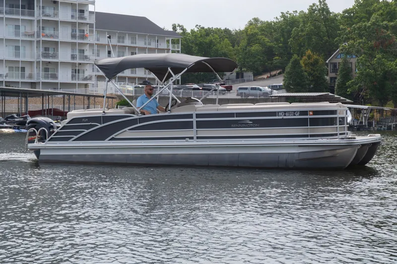 The Image of 2017 Bennington R25 pontoon boat cruising on a lake near waterfront buildings. - 0