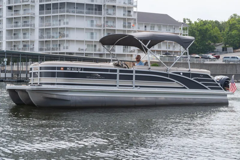 Slide: The Image of 2017 Bennington R25 pontoon boat cruising on a lake near waterfront buildings. - 2