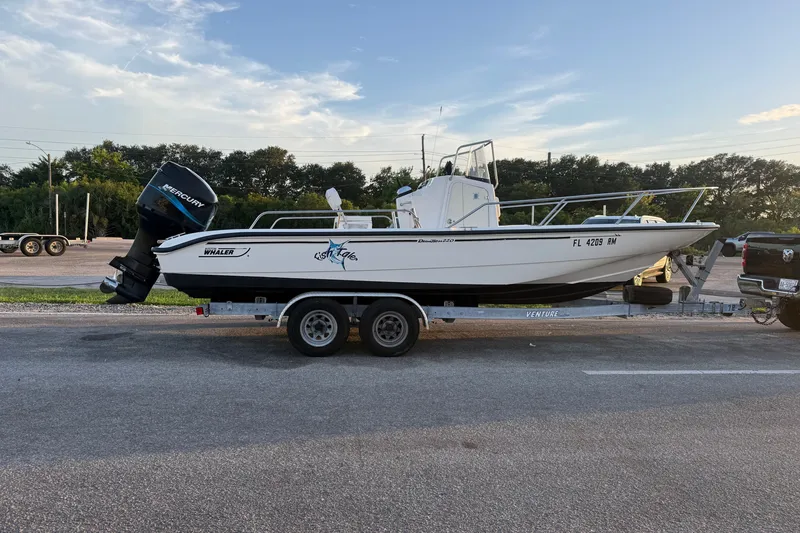 The Image of 2003 Boston Whaler 220 Dauntless boat on trailer, parked outdoors, with Mercury outboard motor. - 0