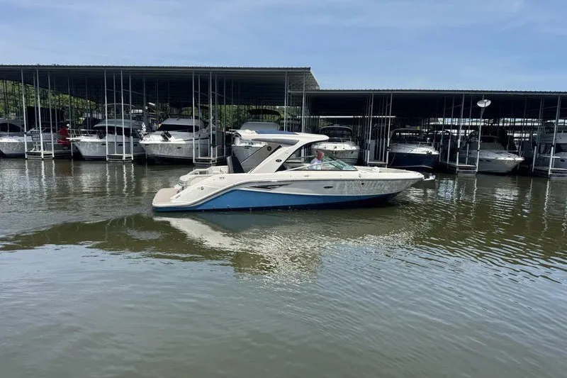 Slide: The Image of 2022 Sea Ray SLX 310 boat cruising near marina docks on a sunny day. - 2