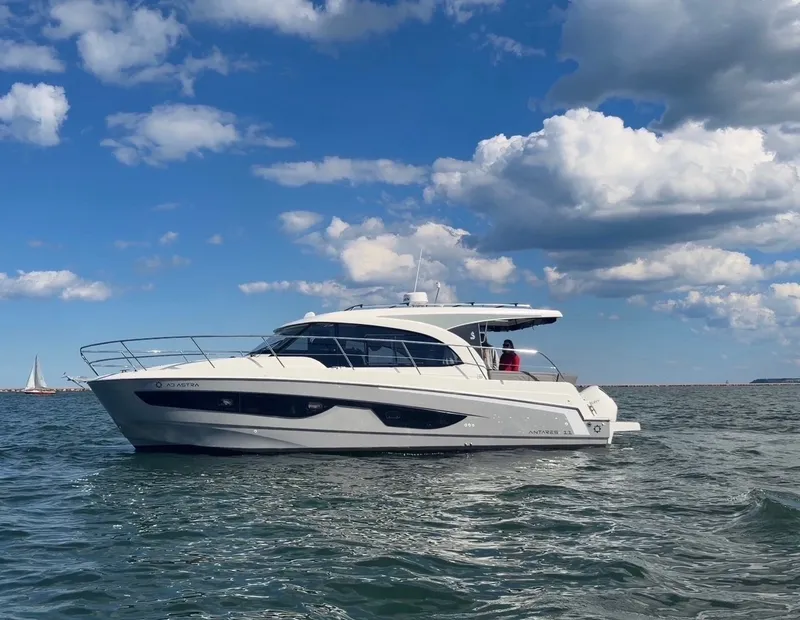 The Image of The 2025 Beneteau Antares 11 cruises on calm waters under a blue sky with clouds. - 0