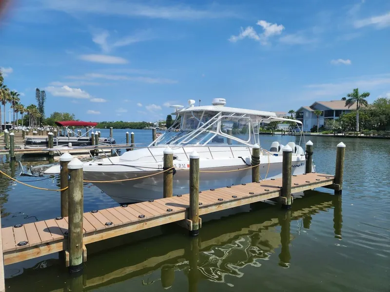 The Image of A white 2004 Pro-Line 30 Express Walkaround boat docked at a wooden pier in a calm harbor. - 2