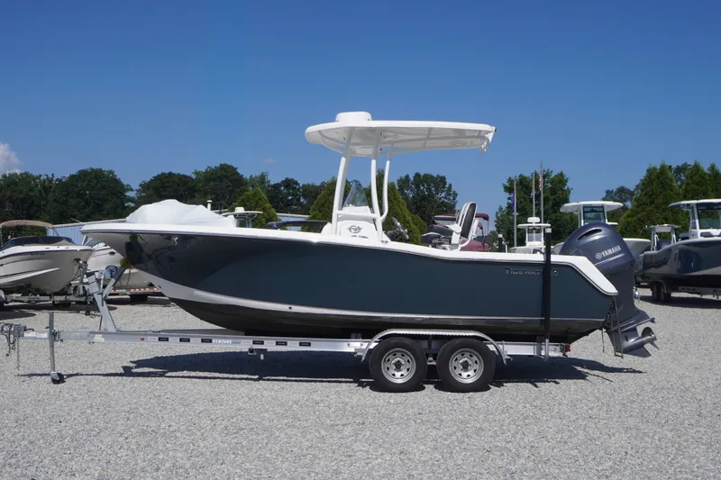 The Image of 2023 Tidewater 220 CC Adventure boat on trailer, parked outdoors under clear blue sky. - 0