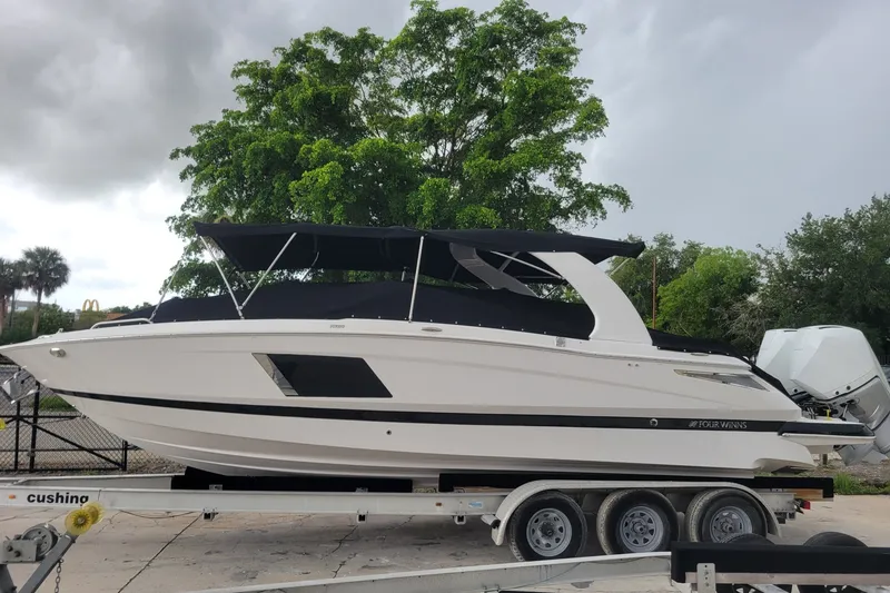 Slide: The Image of 2019 Four Winns H290 OB boat on trailer, parked outdoors with lush greenery background. - 36