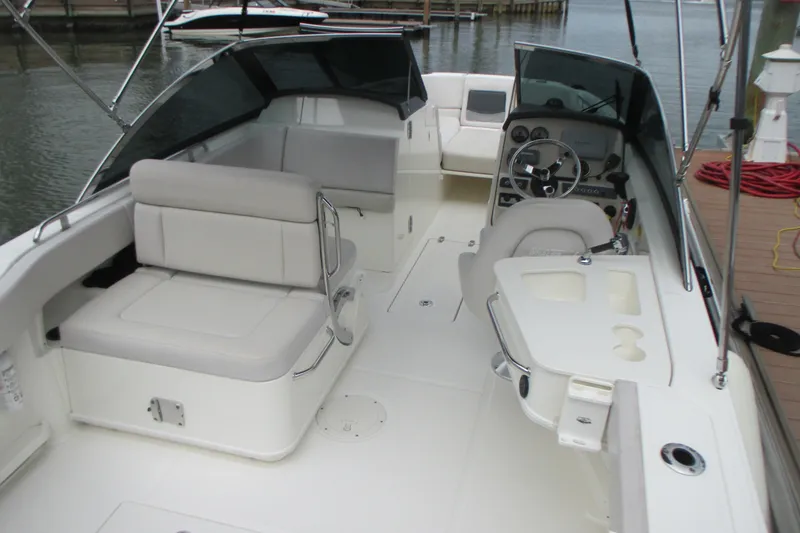 Slide: The Image of 2013 Boston Whaler 230 Vantage boat interior with seating and steering wheel, docked by the water. - 7