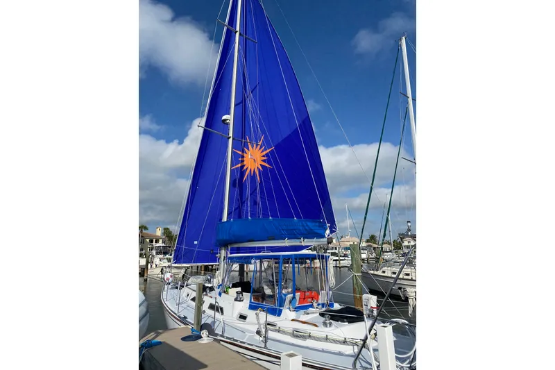 The Image of 1989 Hylas 44 sailboat with vibrant blue sail docked at marina. - 0