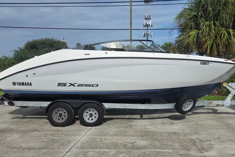 Slide: The Image of 2024 Yamaha Boats SX250 on trailer, parked outdoors with palm trees in background. - 1