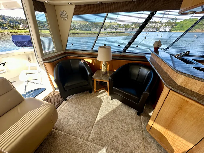 Slide: The Image of Interior of the 1999 Bayliner 4788 with two black armchairs and a table, surrounded by windows. - 19