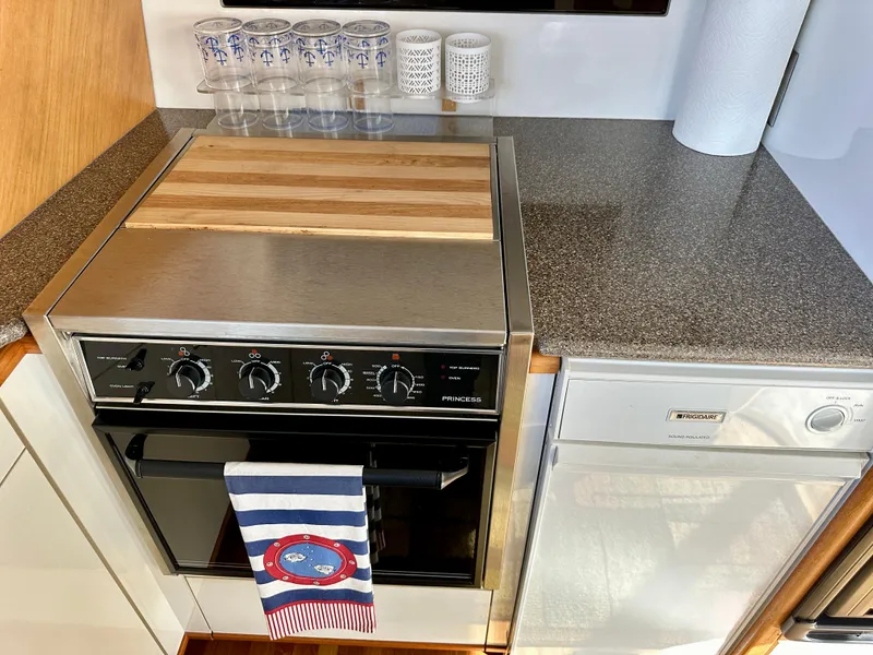 Slide: The Image of The 1999 Bayliner 4788 Pilot House Motoryacht's kitchen features a stove with a wooden cover and a dishwasher. - 33