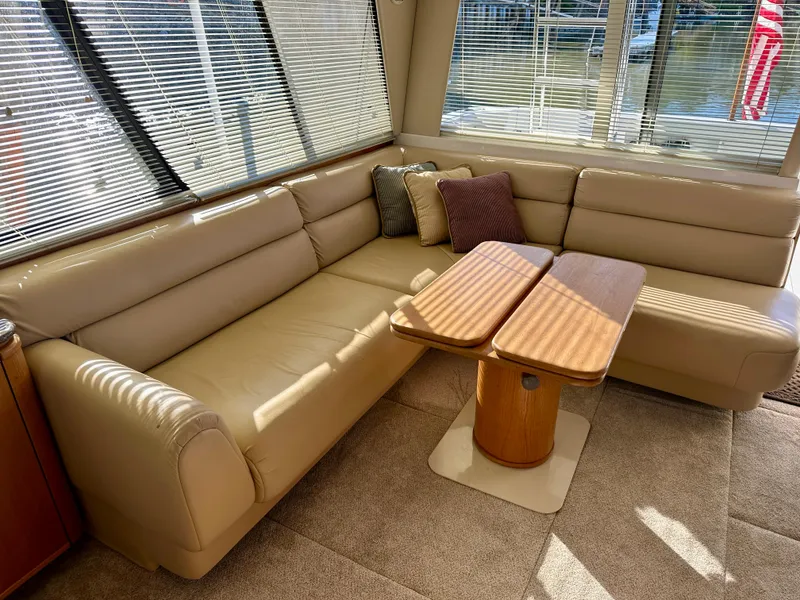 Slide: The Image of The image shows the interior of a 1999 Bayliner 4788 Pilot House Motoryacht with a beige leather couch and wooden table. - 22
