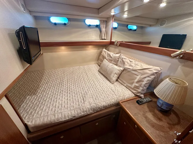 Slide: The Image of The 1999 Bayliner 4788 cabin features a cozy bed, windows, and a TV. - 48