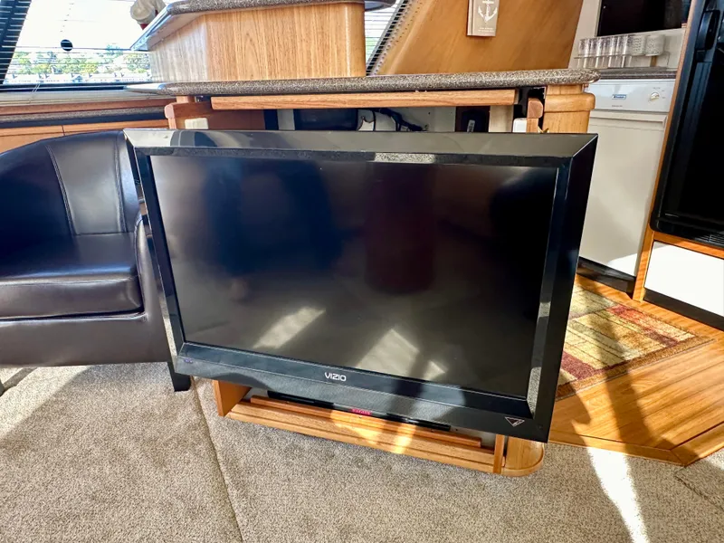Slide: The Image of The interior of a 1999 Bayliner 4788 Pilot House Motoryacht features a large TV and leather seating. - 28