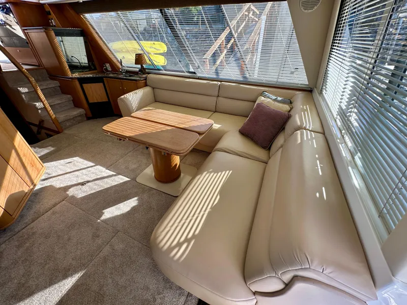 Slide: The Image of The image shows the interior of a 1999 Bayliner 4788 Pilot House Motoryacht with a beige leather couch and wooden table. - 17