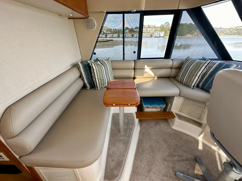 Slide: The Image of Interior of a 1999 Bayliner 4788 with beige sofa, wooden table, and water view. - 13