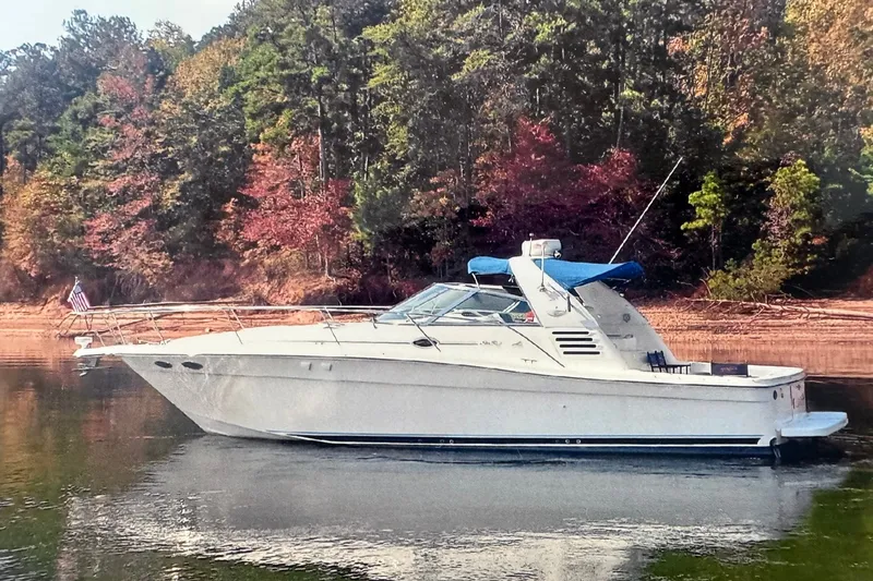 The Image of 1999 Sea Ray 370 Express Cruiser on a serene lake with autumn foliage backdrop. - 0