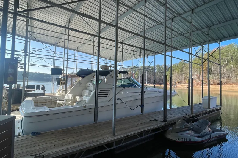Slide: The Image of 1999 Sea Ray 370 Express Cruiser docked under a covered marina with jet skis nearby. - 26