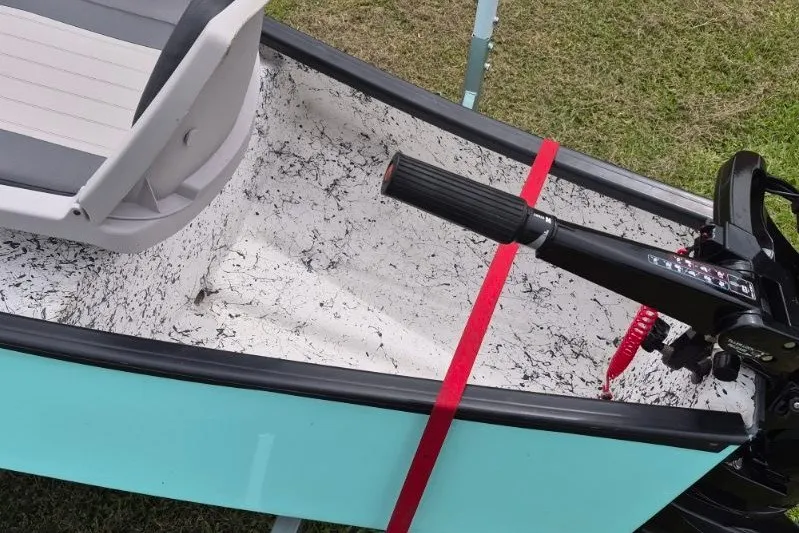 Slide: The Image of 2022 Gheenoe NMZ 15.4 boat interior with motor handle and seat, on grass. - 8
