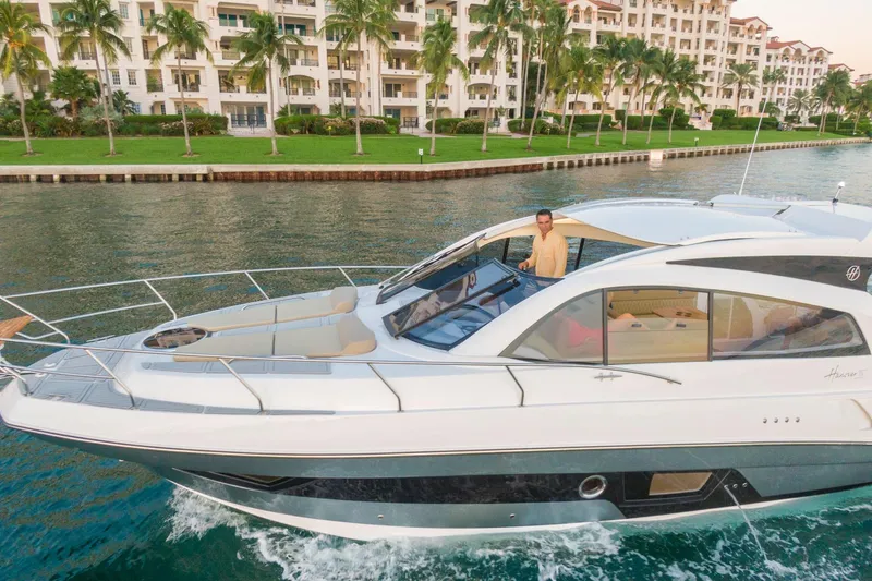 Slide: The Image of Luxurious 2026 Hanover 375 yacht cruising near waterfront apartments with palm trees. - 0