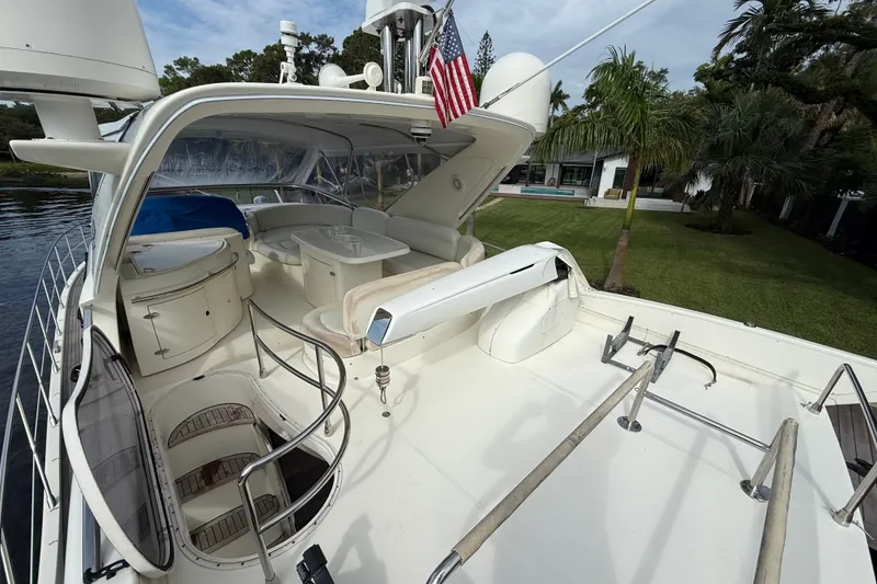 Slide: The Image of 2008 Azimut 62E yacht deck with seating, table, and American flag, near lush greenery. - 13