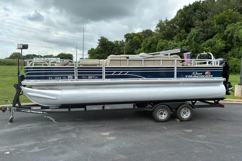 The Image of 2022 Sun Tracker Fishin' Barge 22 DLX pontoon boat on trailer, parked outdoors. - 0