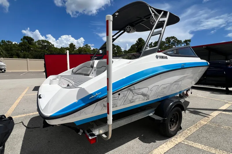 Slide: The Image of 2022 Yamaha AR190 boat on trailer, white and blue design, parked outdoors under clear sky. - 2