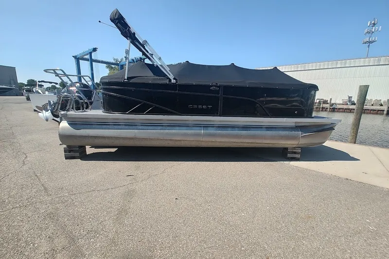 The Image of 2024 Crest 220SLC Classic LX pontoon boat with black cover, docked on a sunny day. - 0
